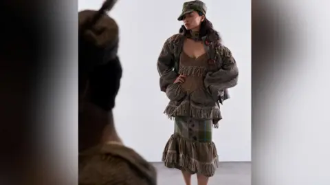 Paul Sunga and Nicky Chan A woman model posing with one of Alexandra's designs created for the Redress Design Award. Top, skirt and jacket are made from undyed or naturally dyed woollen tweed and offcuts rescued from a closing blanket mill. Another model is also partially seen.