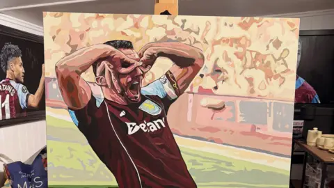 Sue Verity Art A painting of ohn McGinn, a footballer in an Aston Villa shirt has his mouth open and her hands in circles over his eyes