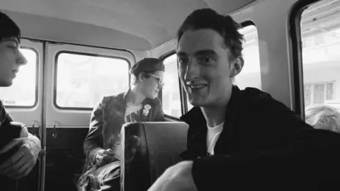Erica Echenberg via Getty Images Black and white photo of members of punk band The Damned sit in the back of their Ford Transit tour van, France, October 1977. L-R Dave Berk, Captain Sensible, Lu Edmonds. (Photo by Erica Echenberg/Redferns)