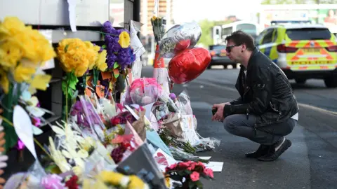 Getty Images A man looks at tributes to the victims of the Manchester Arena attacks. He is crouched down and we view him from the side