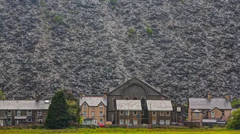 Getty The slate landscape of Blaenau. In front of the old slate clifftops is a row of terraced houses with pitched roofs.