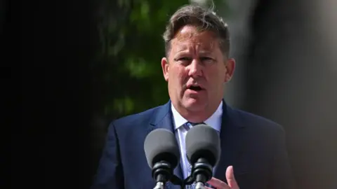 Getty Images Ireland's Transport Minister Darragh O'Brien, with short dark grey hair, wearing a light blue shirt and a navy suit. He is standing behind two microphones. 