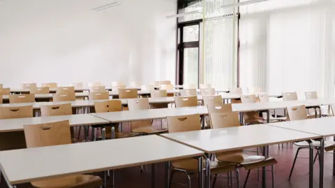Getty Images Rows of empty desks and chairs in a classroom.