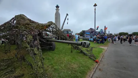 A tank on the left covered in a net. It is on Plymouth Hoe. The sky is grey.