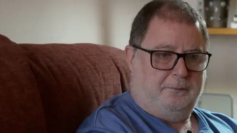 Danny Mendoza wears glasses and blue t-shirt and has grey stubble