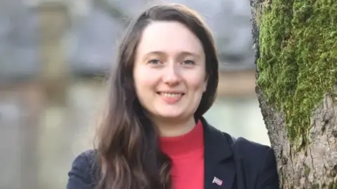 a smiling woman with long brown hair is wearing a black jacket and red top