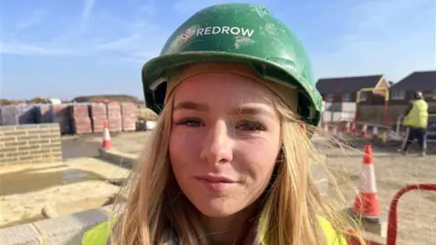 Leeanna - a girl in a green hard hat with blonde hair. You can see her shoulders and she id wearing a hi-viz jacket