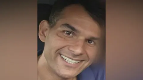 A man with dark hair, wearing a blue top smiling at the camera.