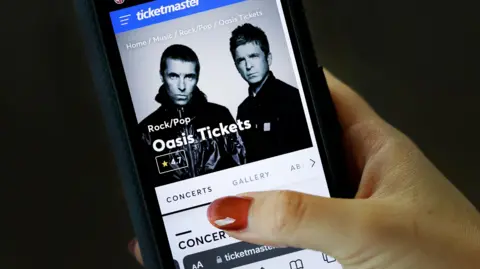 EPA Shot of Ticketmaster website advertising Oasis Tickets on a smartphone, held in a hand with painted red fingernails