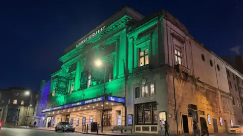 Image shows the Liverpool Empire Theatre on the corner of Lime Street in Liverpool, which was lit up green in honour of The Vivienne who performed there as the Wicked Witch of the West in a Wizard of Oz production in 2024