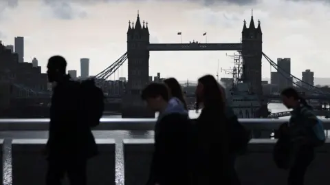Commuters walk across London Bridge in London.
