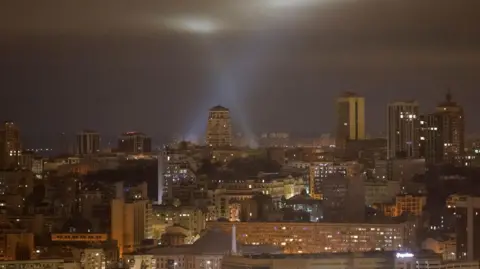 Ukrainian service personnel use searchlights as they search for drones in the sky over Kyiv during a Russian drone strike, 13 January