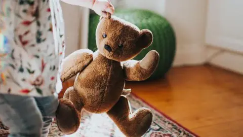A stock image of a toddler holding a teddy bear.
