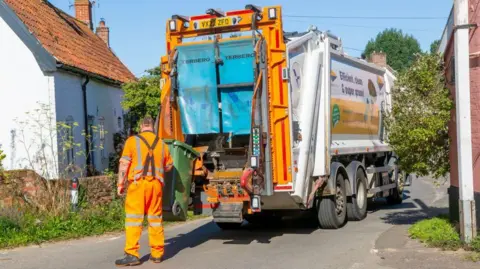 Getty Images A worker wearing an orange high-vis suit empties a bin into a lorry in East Suffolk