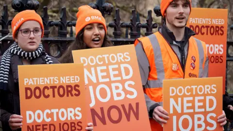 BMA resident doctors hold placards reading 'doctors need jobs now' while striking in London in December