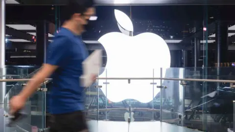 Getty Images An Apple employee walking past an Apple logo