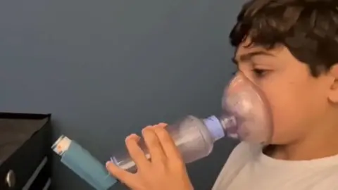 University of Manchester A young child holds an asthma inhaler system over his mouth and nose. There is an air-tight plastic mask connected to a tube which fits over his mouth. This in turn is connected to the inhaler.