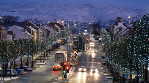 Pascal Diamond Snow on the hills behind Cookstown. a dual carriageway runs through the town with Christmas lights on trees lining the roads