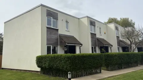 Three white townhouses stand next to eachother. They are two stories high with matching exteriors - white walls and grey finishings with flat roofs. 