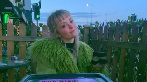 A woman wearing a green jacket, sitting outside.