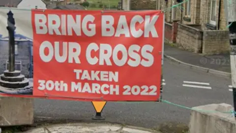 Google A red banner tied over a road that reads: Bring back out cross taken 20th March 2022