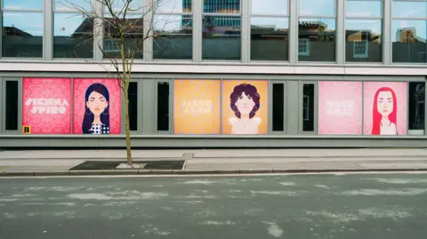 Ellen Offredy Windows displays on an office block featuring three women's faces in cartoon style, in the colours red, yellow and pink. 