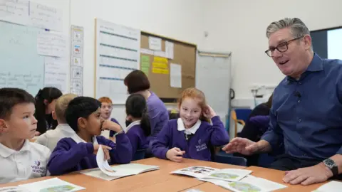 Reuters Britain's Prime Minister Keir Starmer wears a dark blue shirt and reads with pupils during a visit to Welland Academy, to talk about the importance of free school meals and tackling the cost of living. 