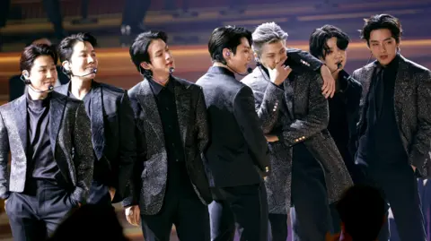 BTS on stage at the Grammy Awards, they are all wearing black glittery suits
