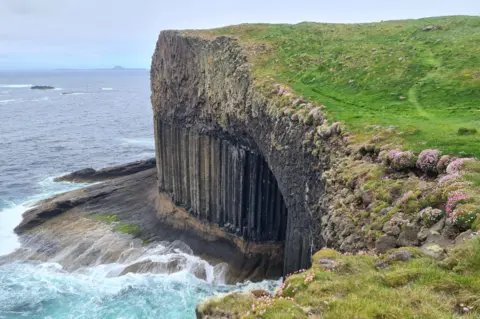 NTS Looking down on waves crashing into a cliff face and the entrance to Fingal's Cave.