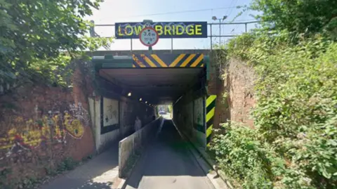 A view of the Cow Lane Underpass on a sunny day. A sign Low Bridge stands over it.
