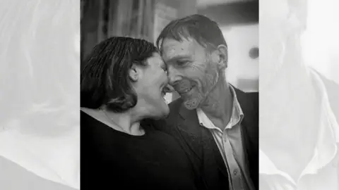 Family handout A man and a woman in a loving pose, touching their faces together in a black and white picture. The man is wearing a dark blazer and light shirt, the woman is wearing a black top.