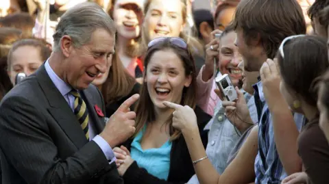 AP Charles laughs and chats with students. He points a finger at one student, as they take his photo