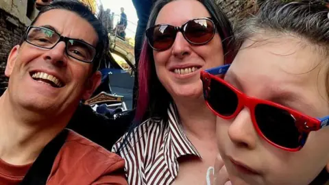 Supplied The photo is a selfie taken by Dave who is wearing black rimmed glasses and an orange top. Next to him is his wife Emma who is wearing sunglasses and a striped shirt. next to her is Robin who is wearing spider man sunglasses.