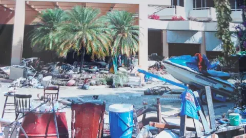 Richard de Gottal A street lined with buildings and palm trees which is filled with debris and a jet ski