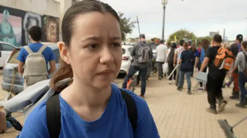 Amparo Esteve wearing a blue t-shirt and a rucksack talks to the camera