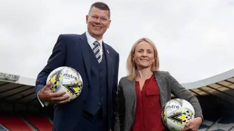 SNS Neil Doncaster, izquierda, y la directora ejecutiva de SWPL, Fiona McIntyre, derecha, sosteniendo balones de fútbol Mitre.