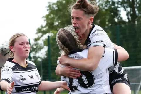 Hull FC Three women rugby players in black and white strips celebrating.