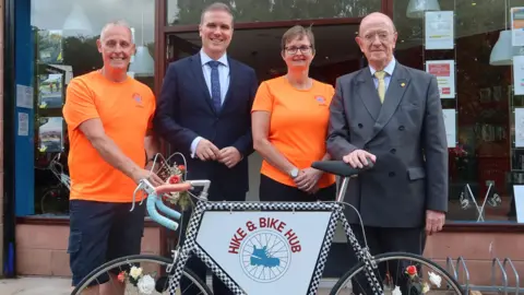 A group of four stand above a bike which says "hike & bike hub"