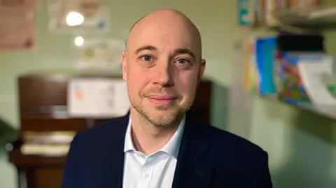 Martin Giles/BBC Head and shoulders image of Adam Taylor wearing a blue suit jacket and white shirt 