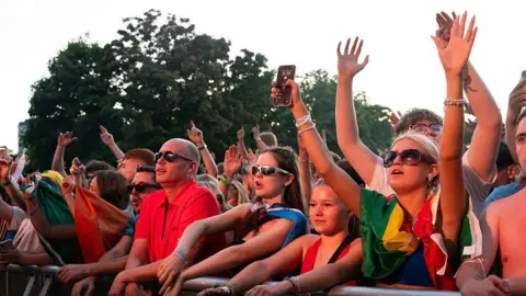 Getty Images Fans watching an act at music festival with several fans raising their arms in the air.