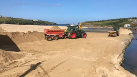 Tractor on a beach with a big pile of sand in its trailer