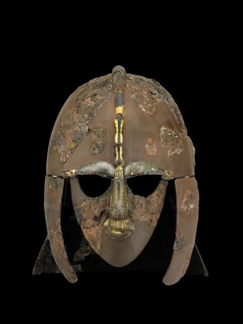 The Trustees of the British Museum picture show an ornate iron helmet, dating to the early AD 600s, this outstanding burial clearly commemorated a leading figure of East Anglia, the local Anglo-Saxon kingdom. It may even have belonged to a king.
