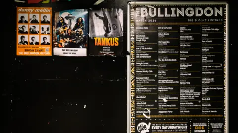 A black wall with posters on it advertising upcoming gigs at The Bullingdon.