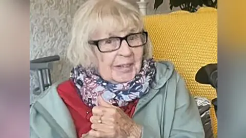 Supplied Victoria Blair is elderly and has grey bobbed hair, glasses and a scarf. She has a hint of a smile on her face, is wearing a scarf and coat. Her hands are clasped together and a gold ring with a diamond are visible. 