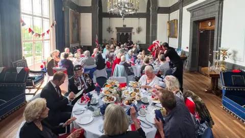 Southampton City Council Dozens of people sitting around large round tables in a grand room decorated with marble, large gold-framed paintings and chandeliers.