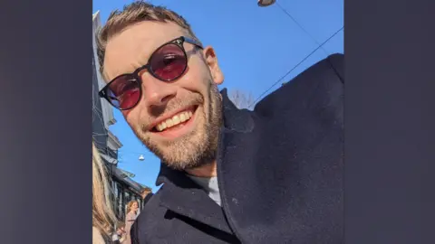 Aran Potkin from Farnham. Aran is wearing sunglasses and has fair hair and a short beard. He is wearing a navy coat.