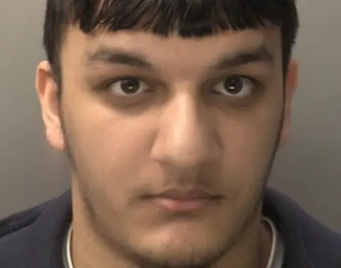 West Midlands Police The face of a man with dark hair is prominent in the image. A grey background is behind him.