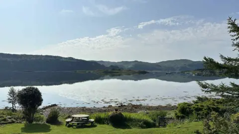 a calm body of water, with a few little boats in it. It is surrounded by greenery.