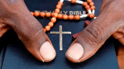 Close-up of hands holding a bible and orange prayer beads