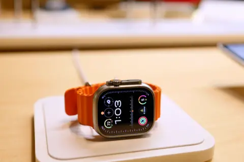Getty Images An black faced Apple Watch with an orange bezel strap, lying on a table. The time reads 1:03.